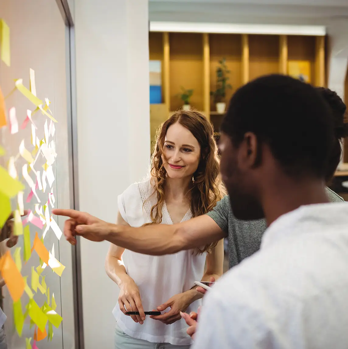 Dos personas trabajando frente a un panel lleno de notas adhesivas
