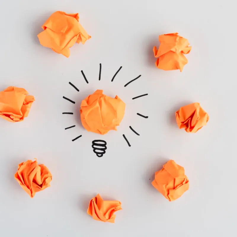 Bolas de papel naranja alrededor de una bombilla dibujada, como ideas en discusión